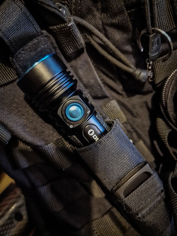 An Olight Seeker 3 Pro torch in it's holster attached to the side of a 5.11 Rush 12 backpack via Molle attachments. 